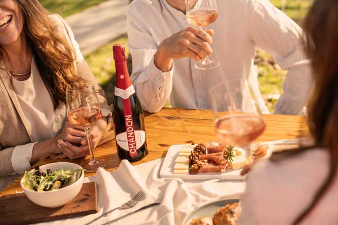 Reunión al aire libre con CHANDON Rosé, aperitivo y tabla de quesos en un día soleado.