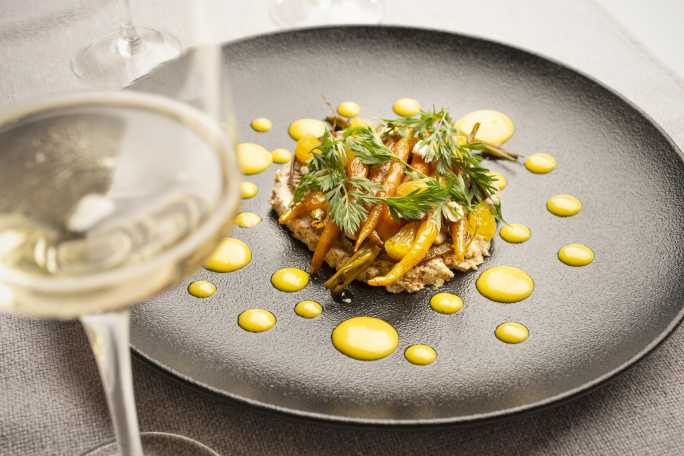 Plato gourmet con zanahorias y esferas amarillas, realzado por un espumante CHANDON Brut en copa.