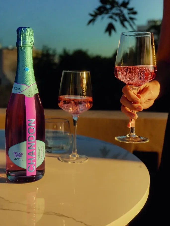 Three friends under a bright blue sky, one holding CHANDON Délice Rosé sparkling wine and two with flutes.