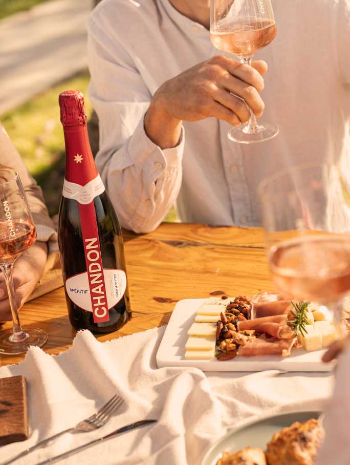 Reunión al aire libre con CHANDON Rosé, aperitivo y tabla de quesos en un día soleado.