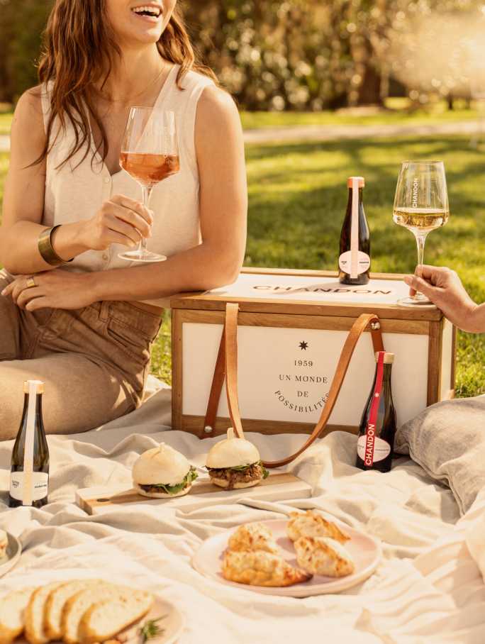 Dos mujeres disfrutando un picnic al aire libre con vino espumoso Chandon y pequeños bocadillos.