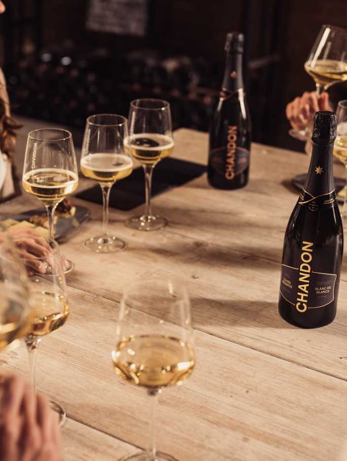 Personas brindan con espumante CHANDON Blanc de Blancs en una mesa de degustación elegante.