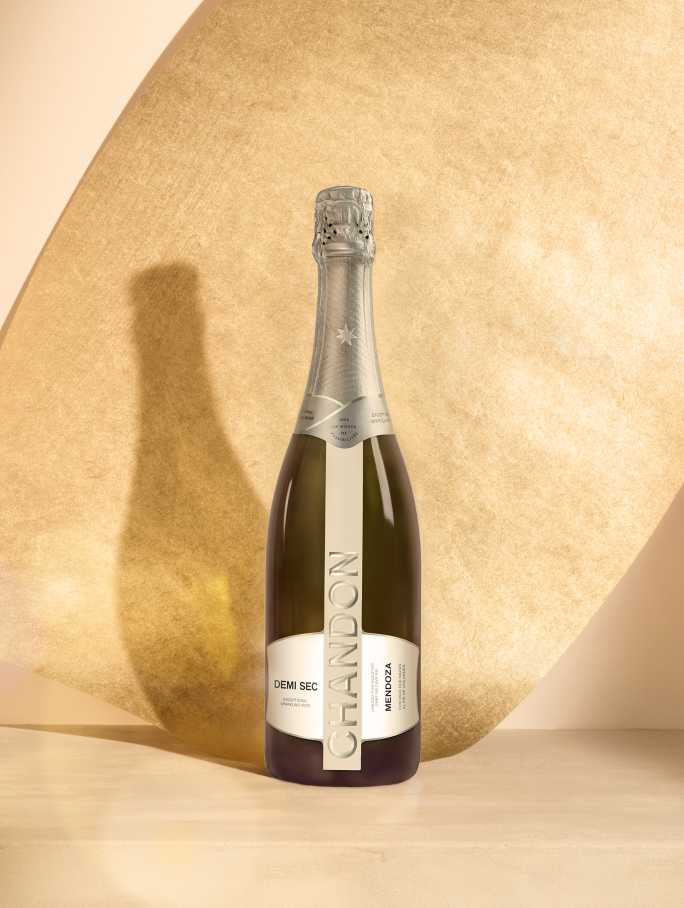 Botella de CHANDON Demi Sec, espumante dulce de Mendoza, reflejada sobre una superficie clara con fondo ocre.