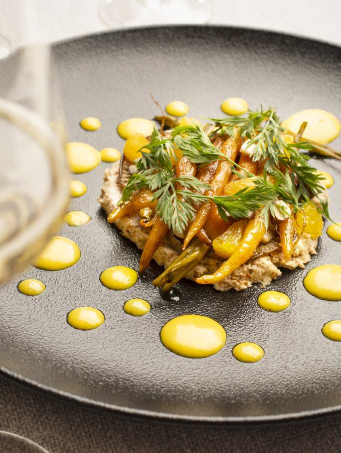 Plato gourmet con zanahorias y esferas amarillas, realzado por un espumante CHANDON Brut en copa.