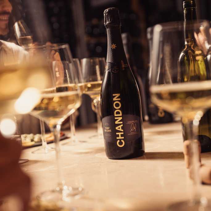 Botella de Chandon Brut Nature sobre mesa con copas de espumante.