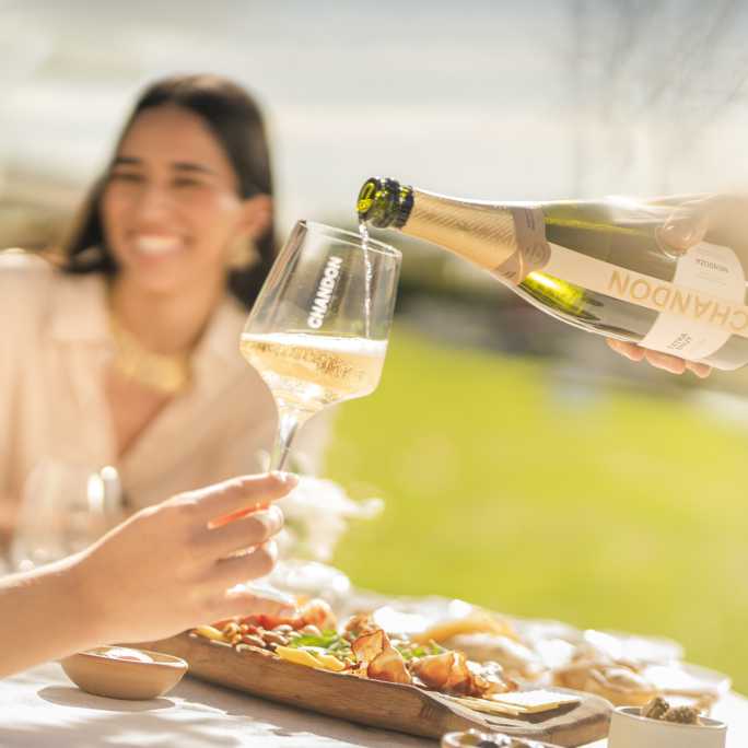 Sirviendo Chandon Extra Brut en copas durante un almuerzo al aire libre en Mendoza.