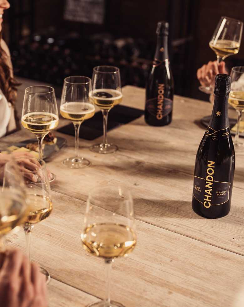 Personas brindan con espumante CHANDON Blanc de Blancs en una mesa de degustación elegante.