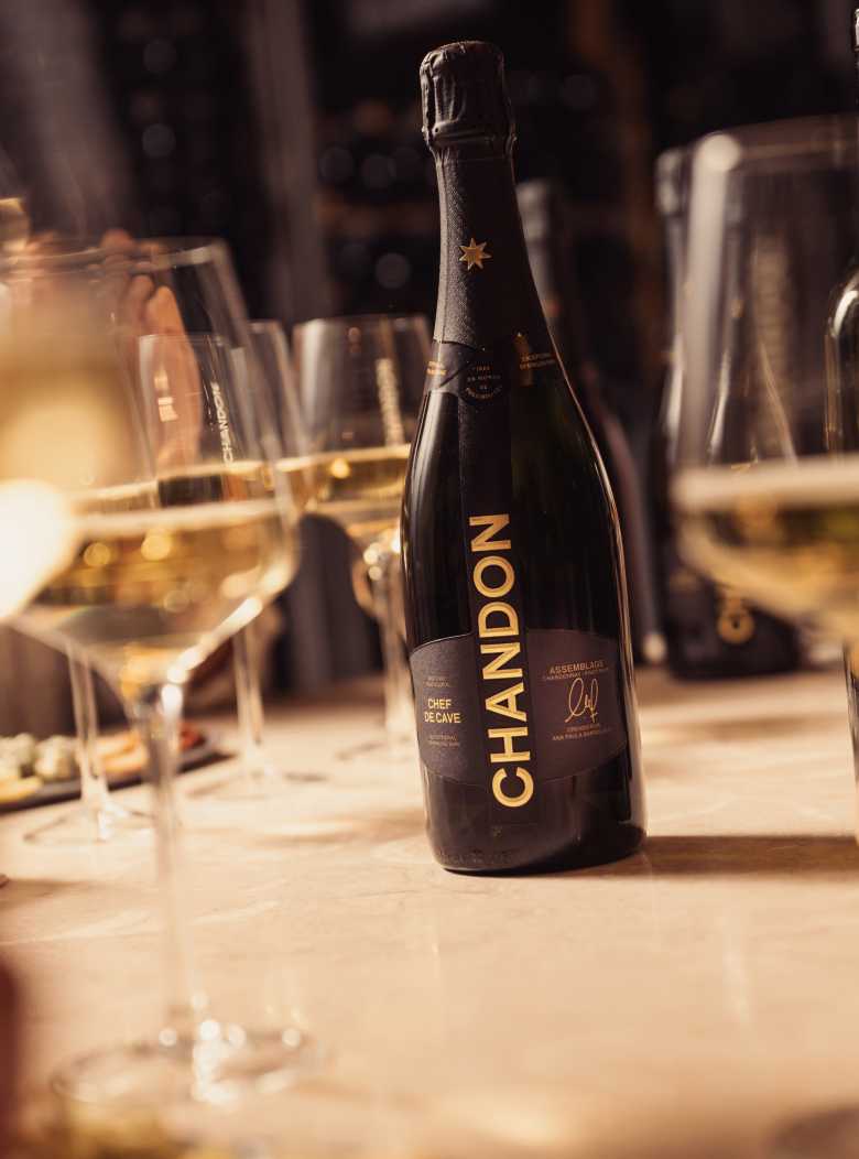 Botella de Chandon Brut Nature sobre mesa con copas de espumante.