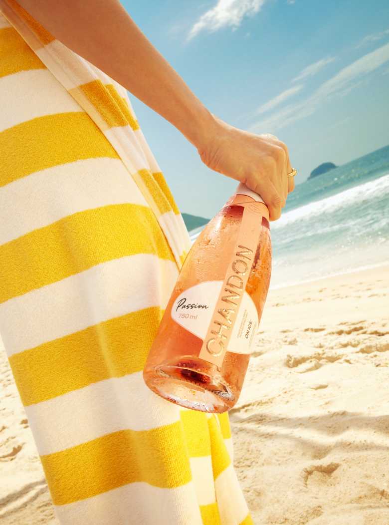 Mulher na praia segurando uma garrafa de CHANDON Passion