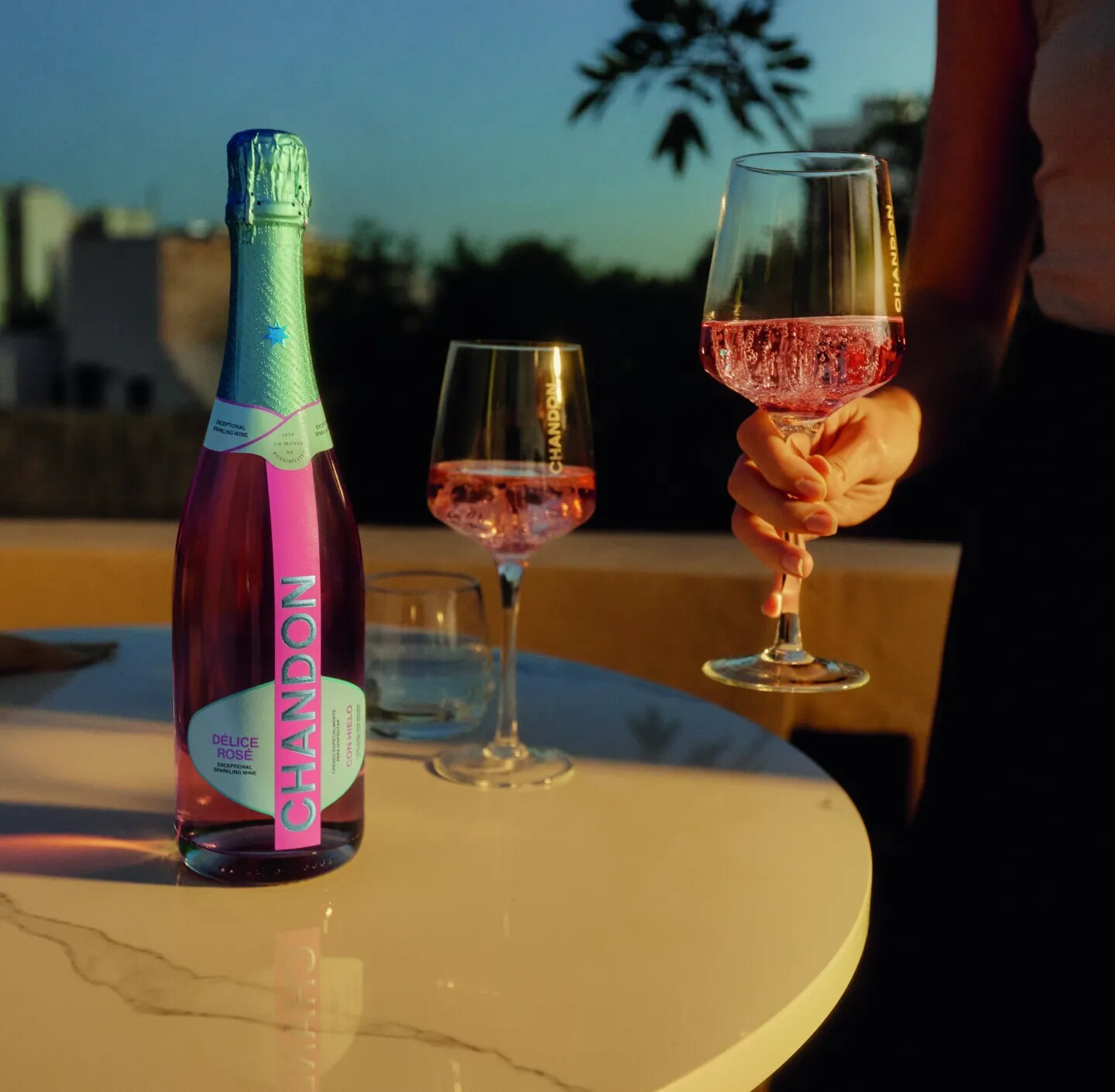 Three friends under a bright blue sky, one holding CHANDON Délice Rosé sparkling wine and two with flutes.