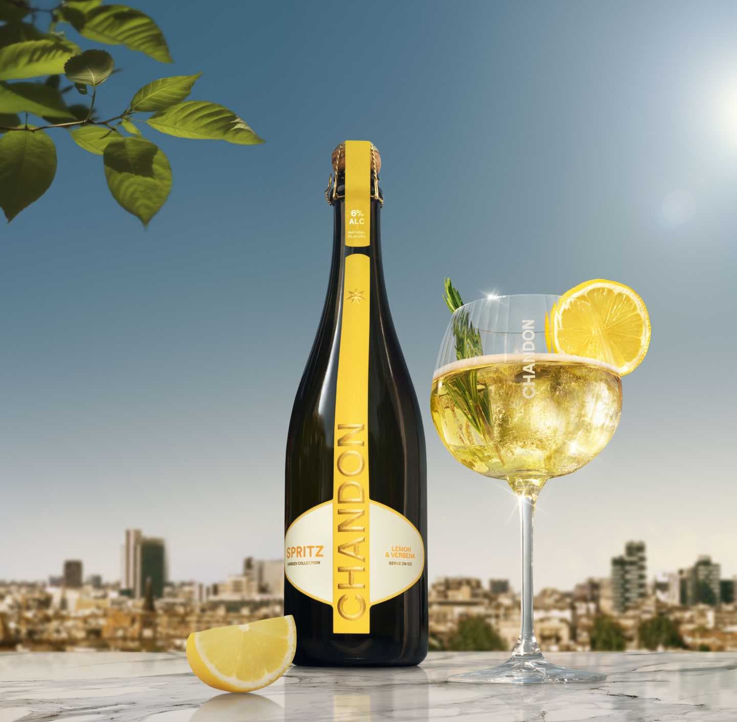 A bottle of Chandon Spritz Lemon & Verbena next to a glass of Chandon Spritz cocktail garnished with a lemon slice and a sprig of rosemary, set against a sunny cityscape background.