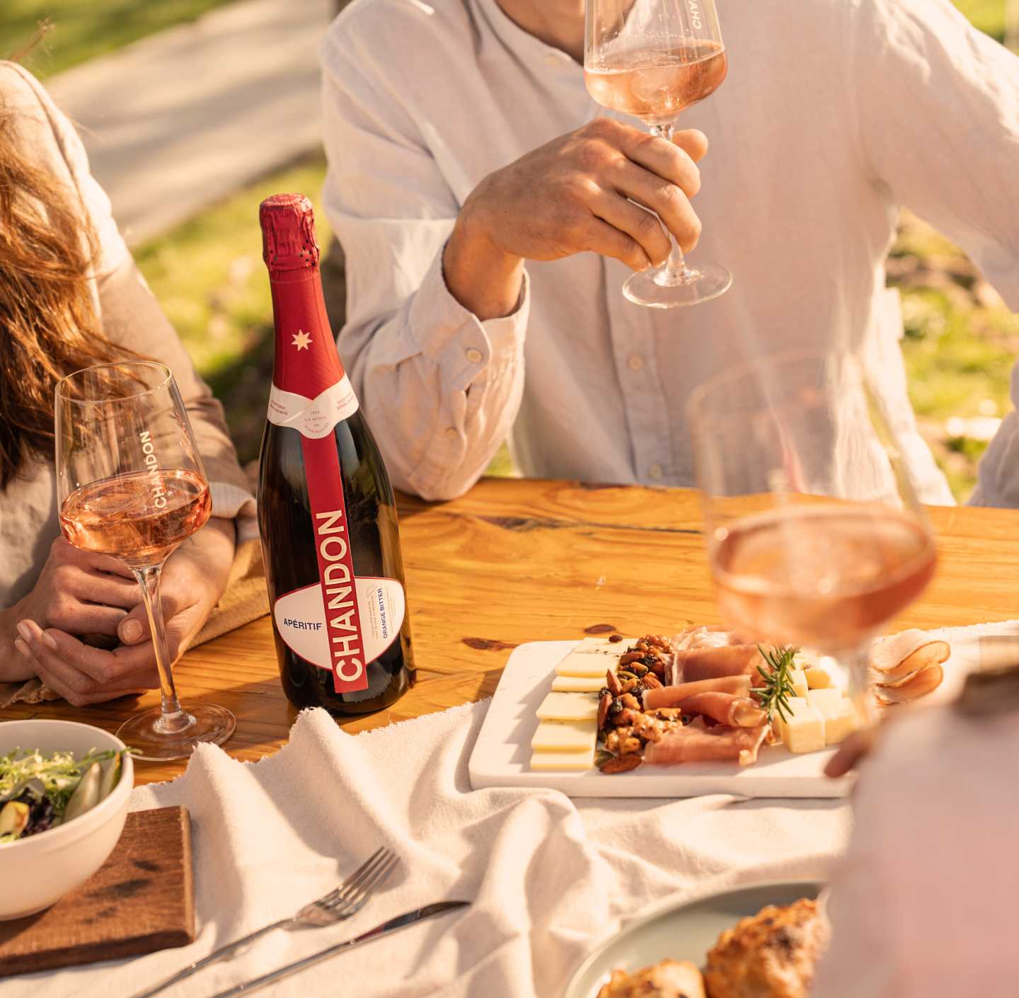 Reunión al aire libre con CHANDON Rosé, aperitivo y tabla de quesos en un día soleado.