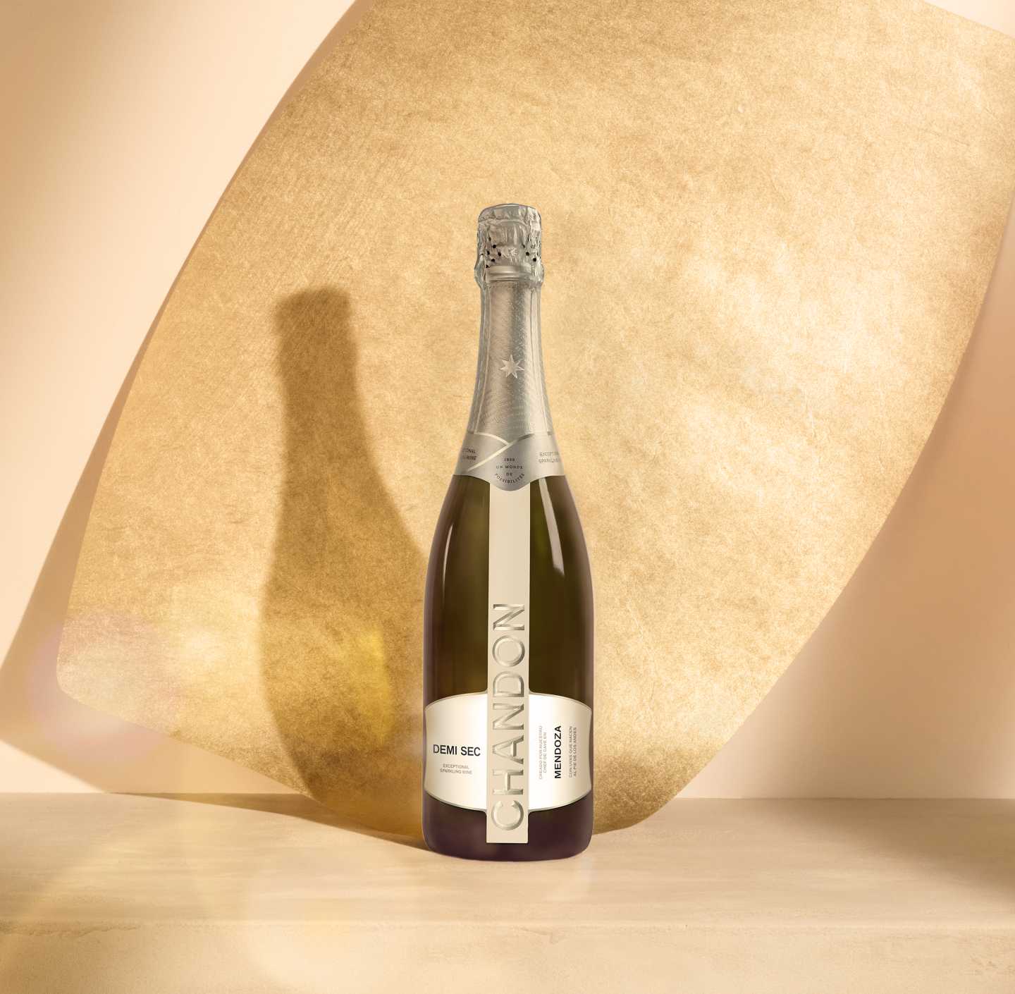 Botella de CHANDON Demi Sec, espumante dulce de Mendoza, reflejada sobre una superficie clara con fondo ocre.