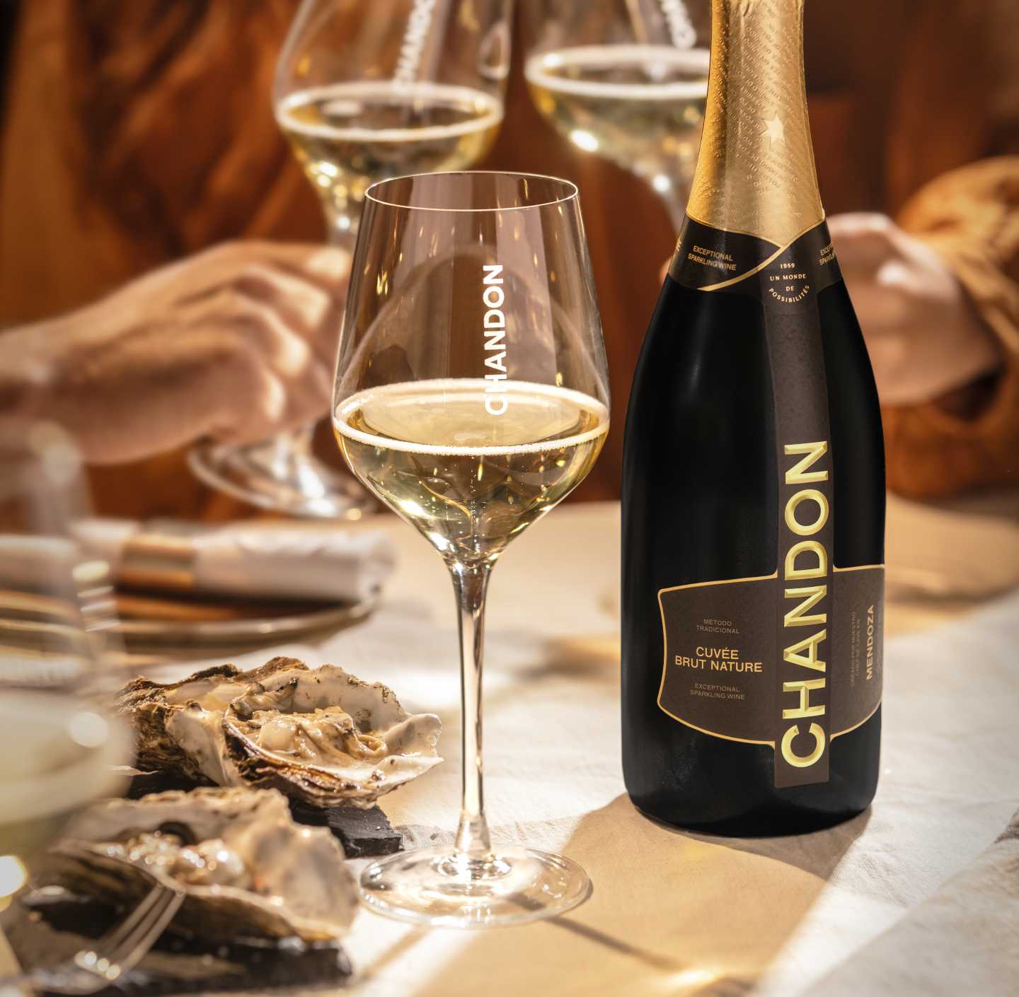 Botella de CHANDON Cuvée Brut Nature, copas de vino espumoso Argentino, y ostras en mesa.