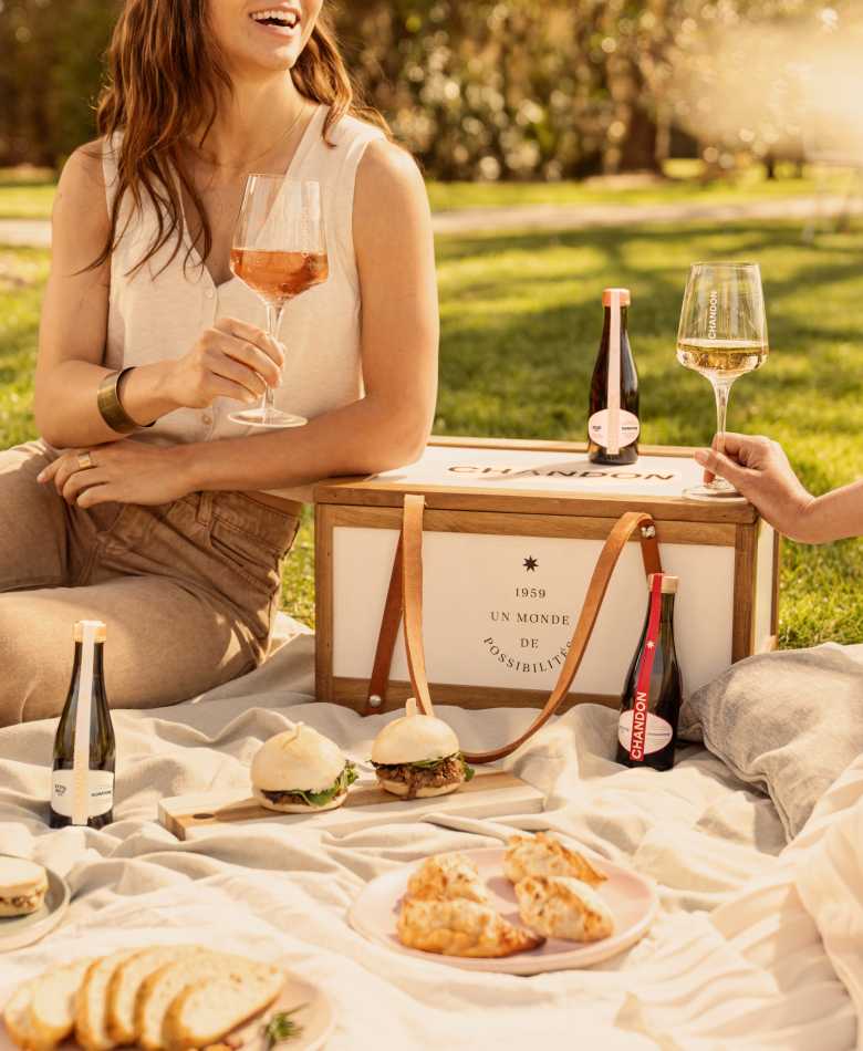 Dos mujeres disfrutando un picnic al aire libre con vino espumoso Chandon y pequeños bocadillos.