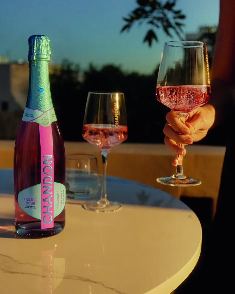 Three friends under a bright blue sky, one holding CHANDON Délice Rosé sparkling wine and two with flutes.