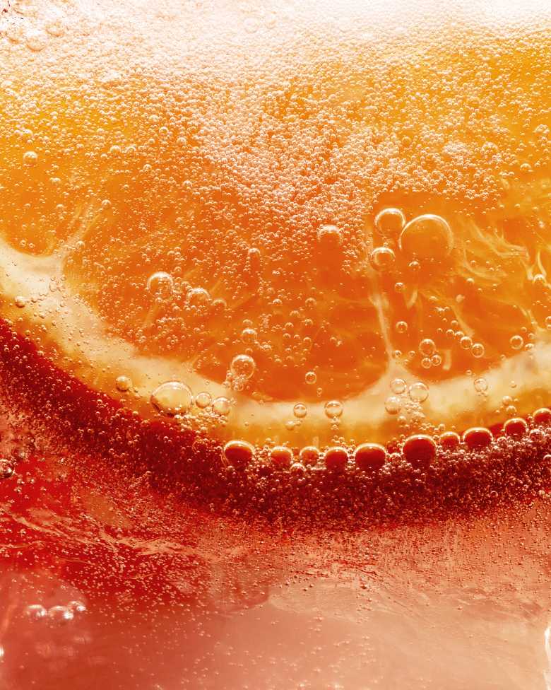 Close-up of an orange slice submerged in a bubbly, orange-hued liquid.