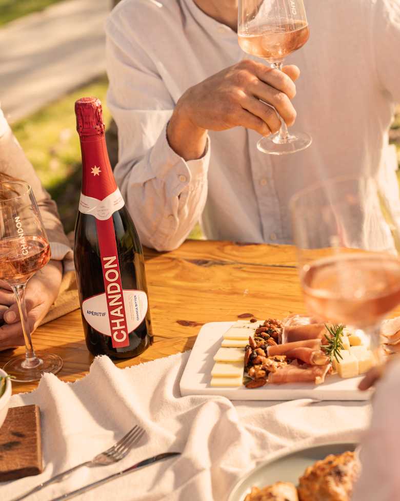 Reunión al aire libre con CHANDON Rosé, aperitivo y tabla de quesos en un día soleado.