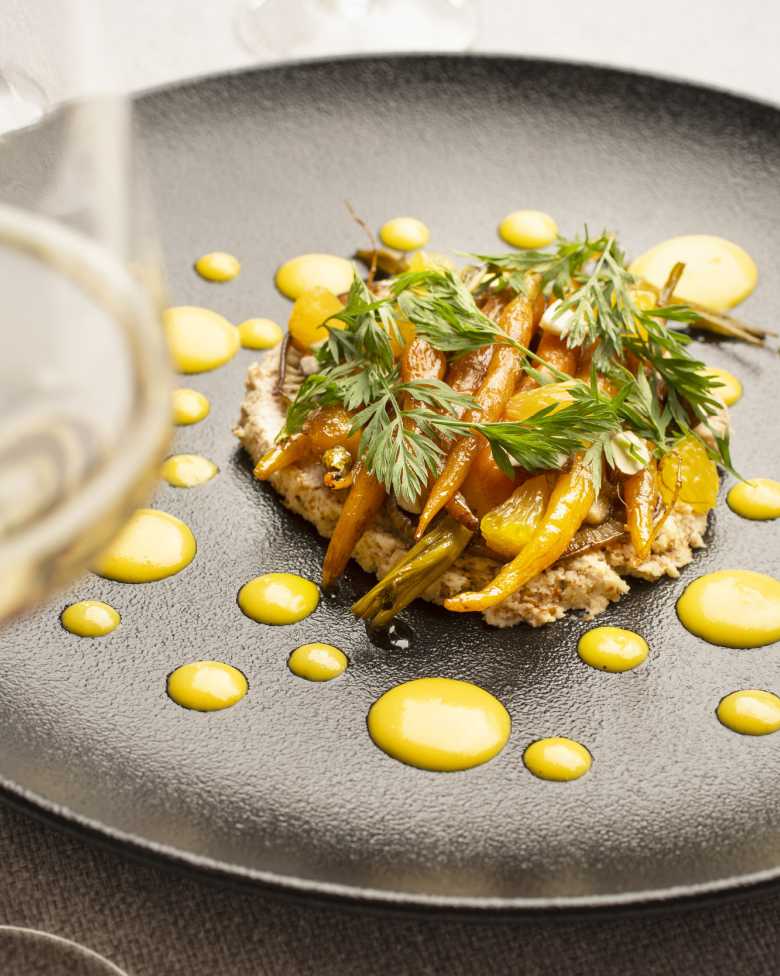 Plato gourmet con zanahorias y esferas amarillas, realzado por un espumante CHANDON Brut en copa.