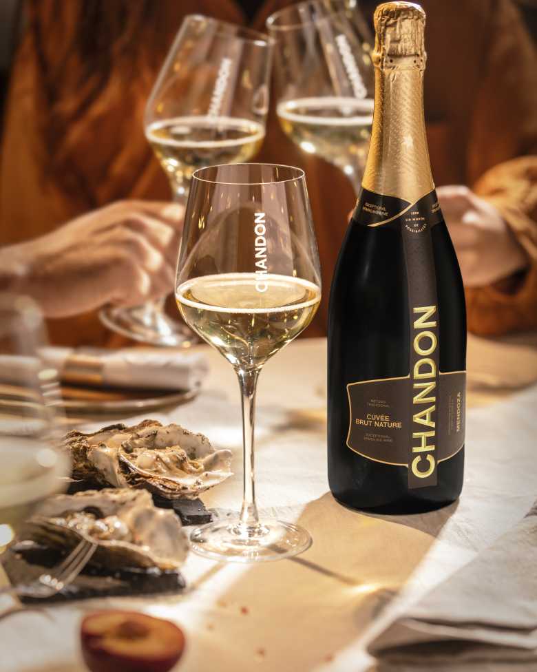 Botella de CHANDON Cuvée Brut Nature, copas de vino espumoso Argentino, y ostras en mesa.