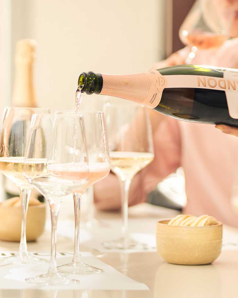 Mujer sirviendo espumante CHANDON Rosé Mendoza en una copa junto a otras botellas.
